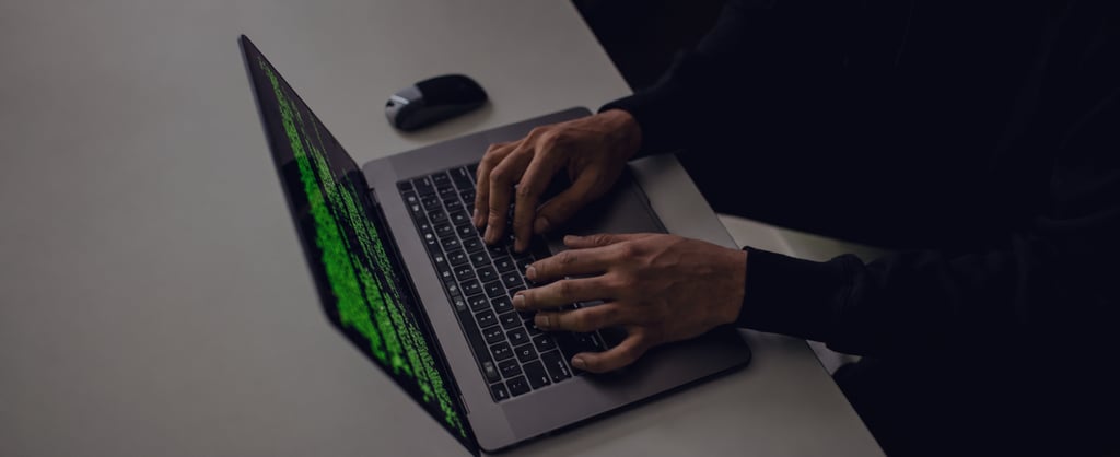 Person typing on a laptop displaying green code on a dark screen, viewed from an overhead angle in a minimalist workspace