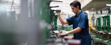 Trabajador operando maquinaria en una planta industrial, representando el Programa de Convergencia Social y Laboral SLCP en entornos de manufactura.