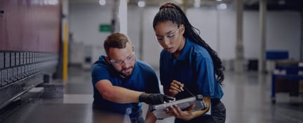 Two factory workers reviewing a tablet in an industrial workshop.