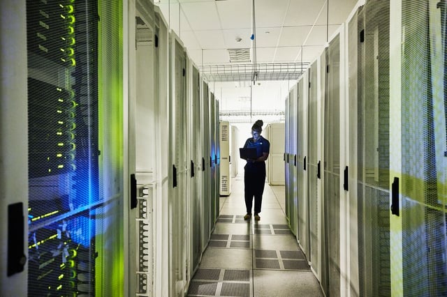 Profissional utilizando laptop em corredor de data center entre racks de servidores