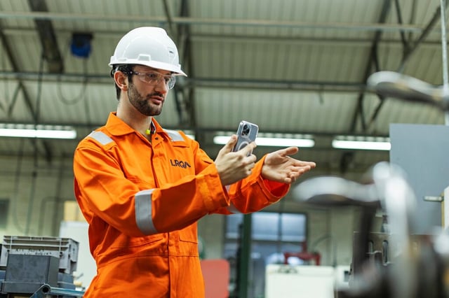 Engineer in safety gear using mobile device to inspect industrial equipment in a manufacturing facility