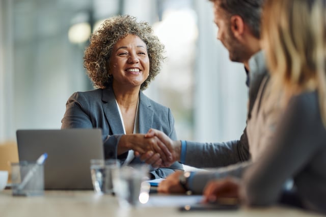 Business handshake in office setting with laptop and observer.