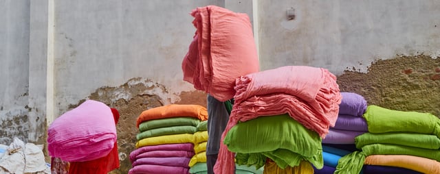 Trabalhadores manuseando e transportando tecidos coloridos empilhados em ambiente de produção