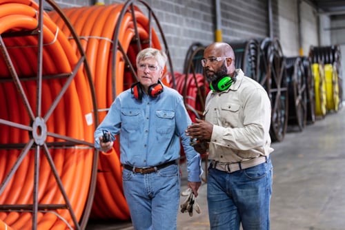 Dois profissionais conversando em instalação industrial ao lado de bobinas de cabos